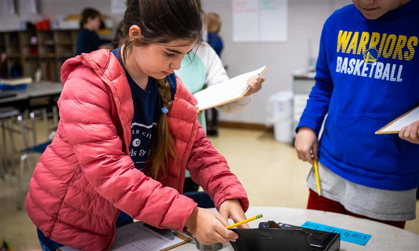 A girl wearing a pink jacket looks at items on a table
